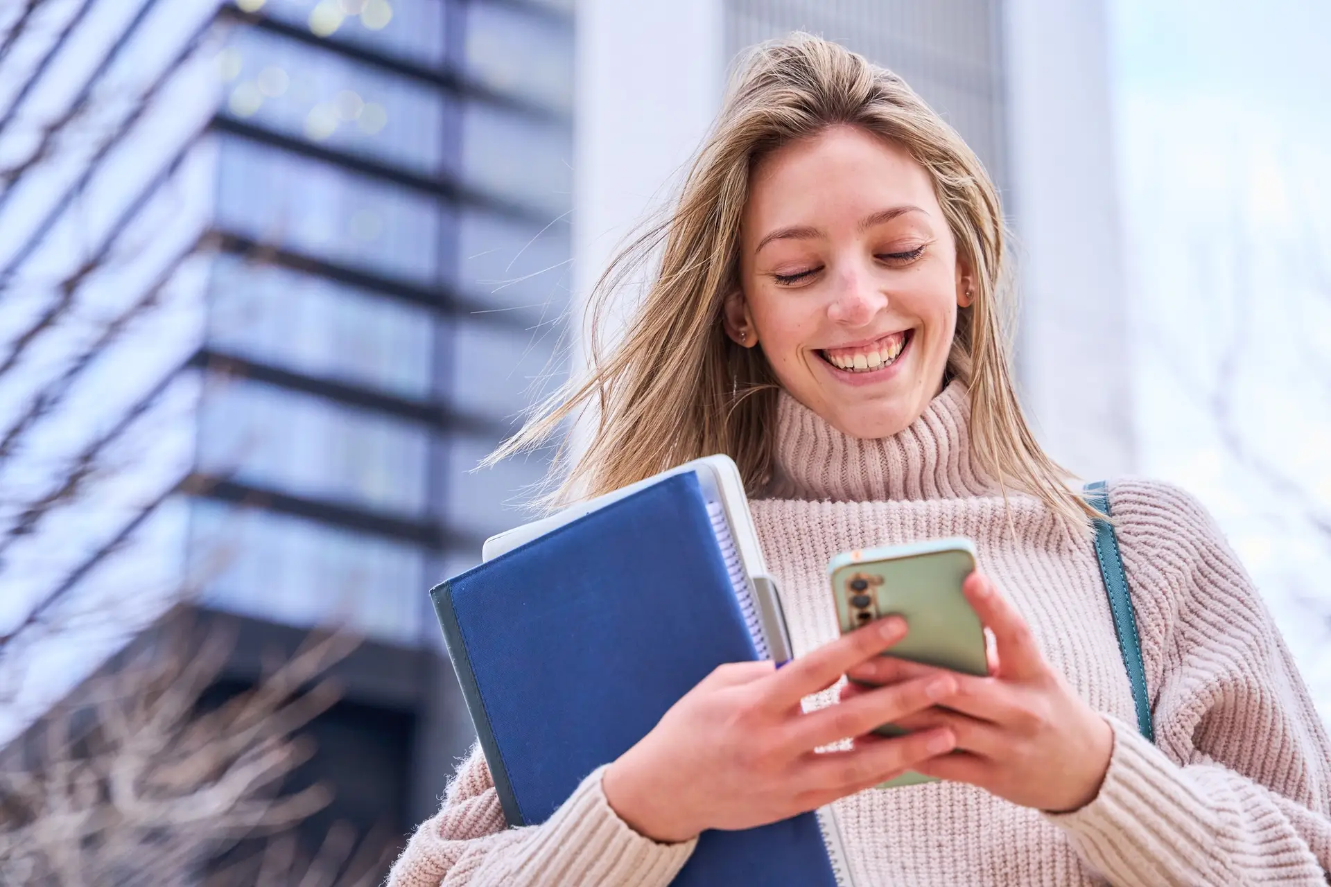 Cheerful Female Student With Smartphone And Workbooks Standing Outdoors